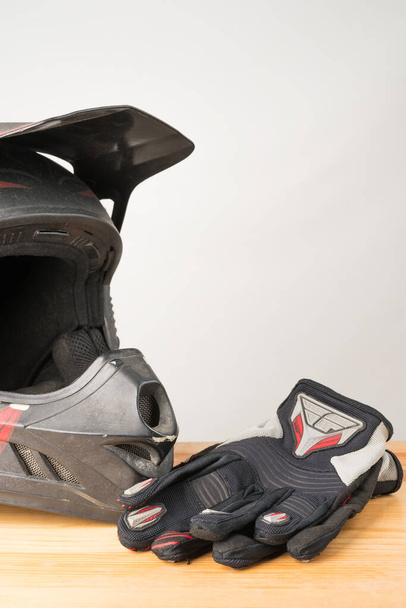Motorcycle protective gear - motocross helmet and gloves on a wooden background. Vertical orientation. Copy space on the top. - Photo, Image