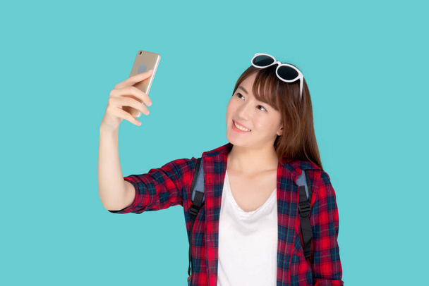 Beau portrait jeune femme asiatique souriant gai et prendre selfie sur téléphone portable intelligent, beauté fille porter voyage été profiter et plaisir en vacances isolé sur fond bleu, concept de vacances. - Photo, image