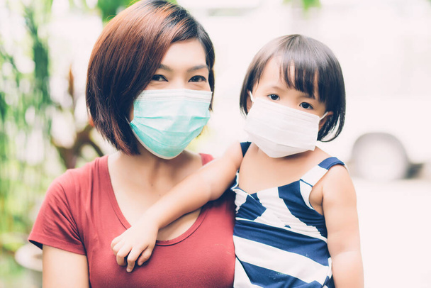 Мать заботиться дочь с маской для лица для защиты болезни гриппа или ковид-19 на открытом воздухе, мама носить медицинскую маску с детской безопасностью для защиты вспышки пандемии, медицинская концепция. - Фото, изображение