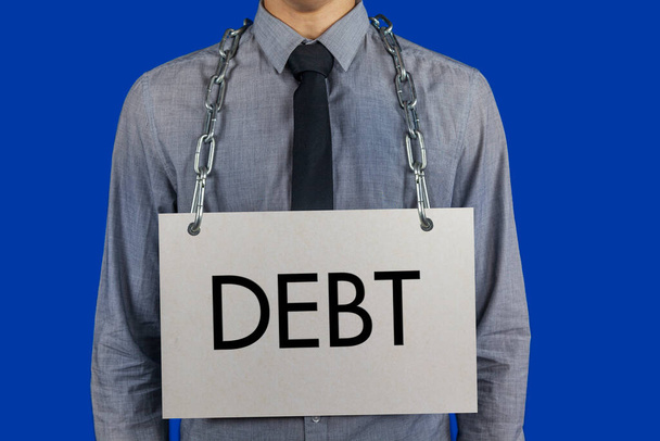 Έννοια: Πίστωση, χρέη, δάνεια. Ένας επιχειρηματίας κρατά μια αλυσίδα γύρω από το λαιμό του με μια αφίσα με την επιγραφή DEBT - Φωτογραφία, εικόνα