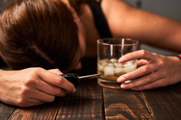 酒のグラスと車の鍵を持った酔った女性の手。アルコール依存症と交通事故の概念. - 写真・画像