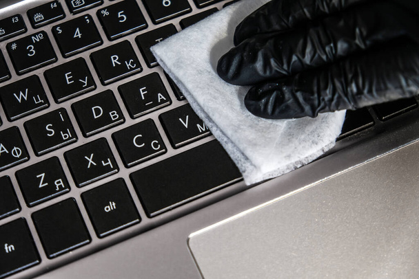 Cleaning the laptop keyboard with antibacterial wet wipes. Black glove and white napkin on a black computer. Removing dust and killing bacteria with hand sanitizer. Personal protection in quarantine. - Photo, Image