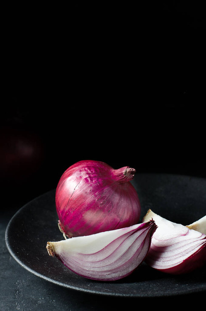 Red onion. Large onion and sliced on a black plate. Black background. Side view. Red onions on old crumpled burlap. Copy space. - Zdjęcie, obraz