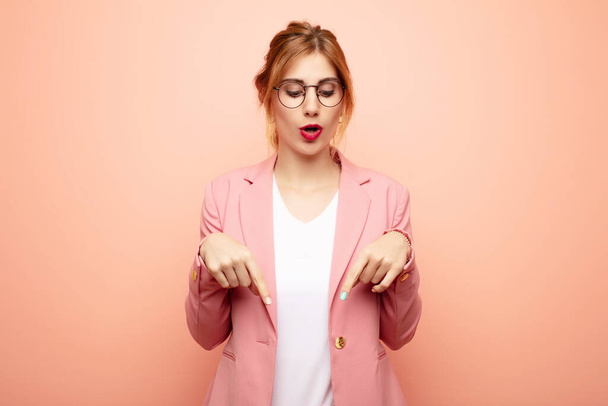 young pretty blonde woman with open mouth pointing downwards with both hands, looking shocked, amazed and surprised. business concept - Photo, image