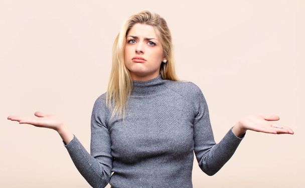 young pretty blonde woman looking puzzled, confused and stressed, wondering between different options, feeling uncertain against flat wall - 写真・画像