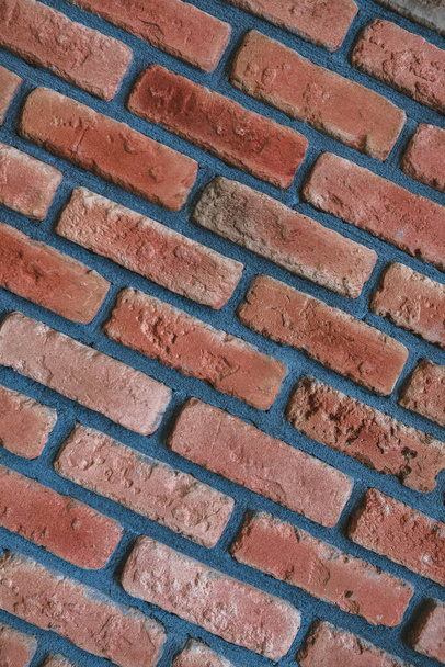 Diagonal front angle of a red brick wall. Close up view of cracked weathered brickwork material. Modern interior design, unique perspective. Loft like room style at home. Rusty cemented block facade. - Photo, Image