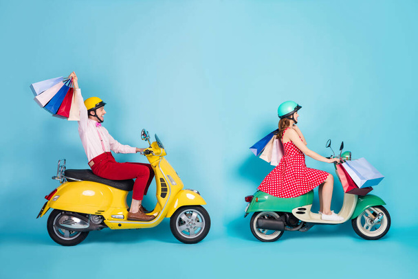 Teljes test profil fotó vicces hölgy srác drive rent retro moped utazók hordoznak sok bevásárló csomag jó hangulat vásárlók külföldön vintage ruhák védő sapkák elszigetelt kék szín háttér - Fotó, kép