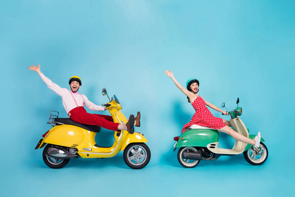 Teljes méretű profil fotó őrült hölgy srác pár vezetni két retro moped utazók forgalmi dugó egyszerű módja elterjedt lábak fel karok szórakozás vintage ruhák sapkák elszigetelt kék háttér - Fotó, kép