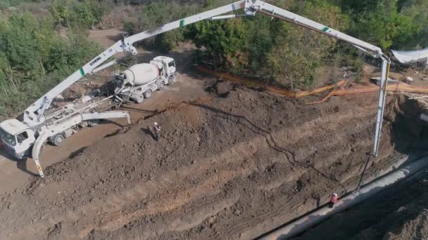 Drohne aus der Luft über Baustelle im Freien geschossen. Ein großer weißer Kran gießt Zement auf die Pipeline-Infrastruktur. Bauarbeiter bei der Arbeit draußen - Filmmaterial, Video