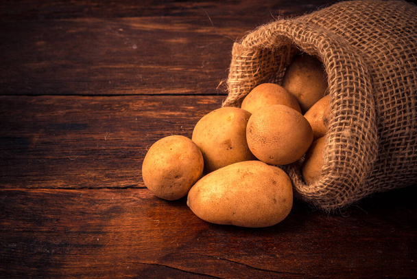 Fresh and raw potatoes in a rustic sack on wooden table - Photo, Image
