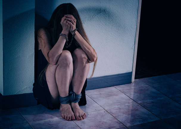 Молодая женщина страдает от насилия, садится на пол, закрывает лицо руками в наручниках. Её руки это вены и шрамы, её ноги связаны верёвкой. посттравматический стресс
 - Фото, изображение