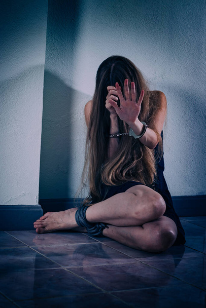 Une jeune femme souffre de violence, s'assoit sur le sol, se couvre le visage avec les mains menottées. Ses mains sont des veines et des cicatrices, ses jambes sont attachées avec une corde. ESPT stress post-traumatique
 - Photo, image