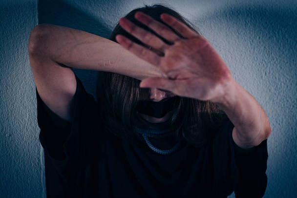 Eine Frau leidet unter Gewalt. Sie sitzt in einem T-Shirt auf einem gefliesten Boden, vergräbt ihr Gesicht und reicht ihre Hand. - Foto, Bild
