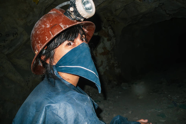 Woman miner with scarf on her face and protective helmet with light in a mine tunnel - Photo, Image