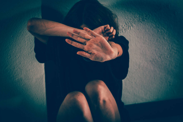 Uma mulher sofre de violência. Ela está sentada em uma camiseta em um chão de azulejos, enterrando o rosto e segurando a mão
. - Foto, Imagem