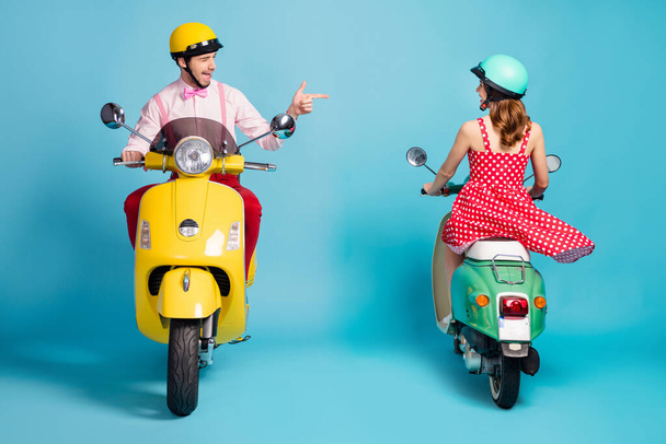 Full body photo of interested guy driving vintage moped blink opposite riding lady flirty handsome meet pretty girl direct finger wear retro clothes headgear isolated blue color background - Valokuva, kuva