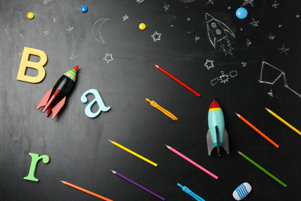 Bright toy rockets, school supplies and drawings on chalkboard, flat lay - Foto, Imagen