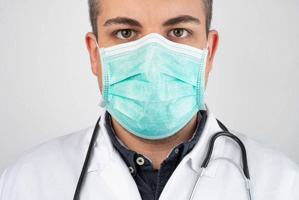 Caucasian man posing as a medical doctor in white overall or scrub with protective face mask and stethoscope around a neck. - Zdjęcie, obraz