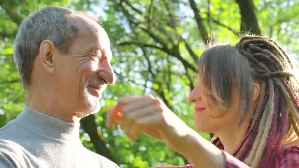 Modern girl with dreadlocks is hugging her senior father spending time together in the park during sunny day. Fathers day concept - Filmagem, Vídeo