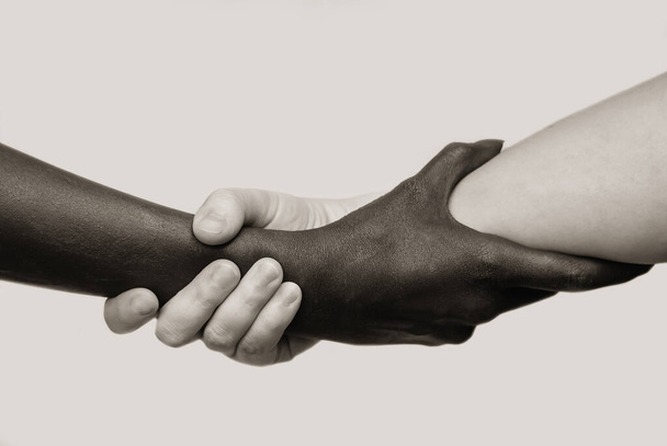 Black-and-white human arms wrapped tightly around each other . The concept of combating racism, friendship and respect .Selective focus, close-up, black and white photography, isolated background - Photo, image
