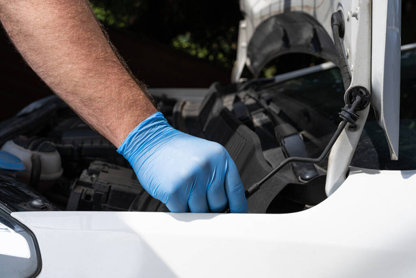 Blanke man in beschermende handschoenenkap of motorkap van een auto. Mechanische reparatie of onderhoud van voertuigen. - Foto, afbeelding