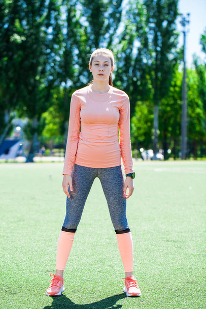 Attractive sporty girl in sportswear doing stretching exercises on stadium. Fitness woman doing warm up workout. - Fotó, kép
