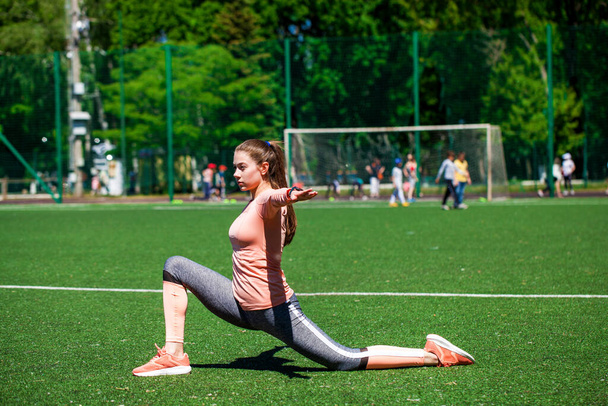 Attractive sporty girl in sportswear doing stretching exercises on stadium. Fitness woman doing warm up workout. - Φωτογραφία, εικόνα