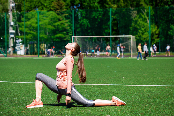 Attractive sporty girl in sportswear doing stretching exercises on stadium. Fitness woman doing warm up workout. - Foto, afbeelding