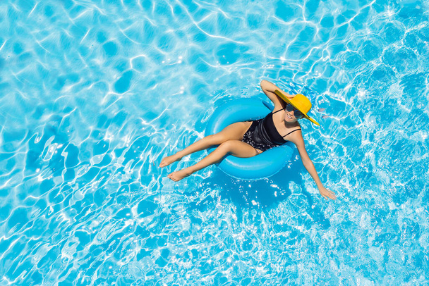Woman sitting in a swimming pool on a ring pool float in a large yellow sunhat - Фото, зображення