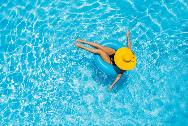 Woman sitting in a swimming pool on a ring pool float in a large yellow sunhat - Photo, Image