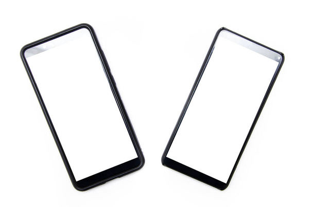Dos teléfonos inteligentes de color negro con una pantalla blanca se encuentran en un fondo blanco cerca, desviados el uno del otro, vista superior e inferior desde un ángulo en macro
 - Foto, Imagen