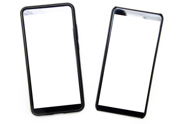 Два смартфона черного цвета с белым экраном лежат на белом фоне рядом, отклоняясь друг от друга, вид сверху и снизу от угла в макросах
 - Фото, изображение