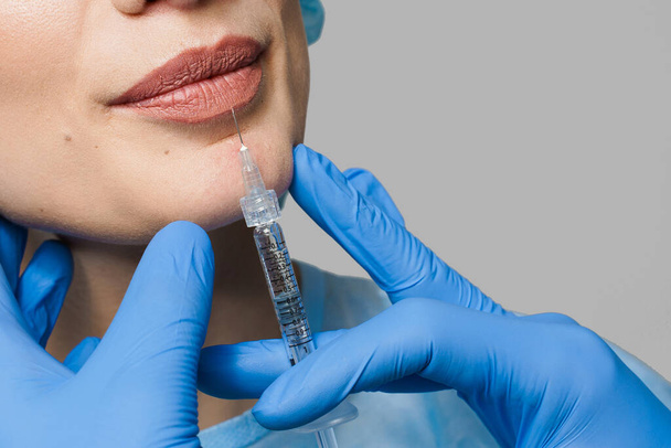 Close-up lippen augmentatie injecties voor aantrekkelijk meisje op witte achtergrond. Plastisch chirurg injecteert in de lip in een medische kliniek. Cosmetische verjongende gezichtsbehandeling. Lege ruimte voor advertenties - Foto, afbeelding