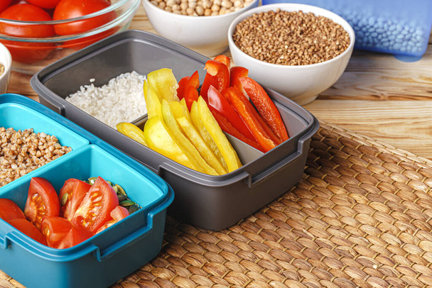 Two lunch boxes with cooked groats and cut vegetables - 写真・画像
