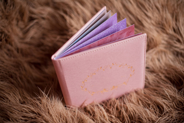Photobook σε ροζ δερμάτινο κάλυμμα βρίσκεται σε καφέ γούνα. Ελεύθερος χώρος για τίτλο, ανοιγμένες σελίδες - Φωτογραφία, εικόνα