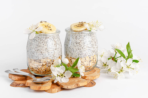 Chia semínko pudink s jogurtem a oves na bílém pozadí zdobené květinami. Superfood koncept. Kopírovat prostor - Fotografie, Obrázek