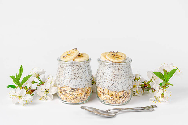 Pouding aux graines de chia avec yaourt et avoine sur fond blanc décoré de fleurs. Concept Superfood. Espace de copie
 - Photo, image