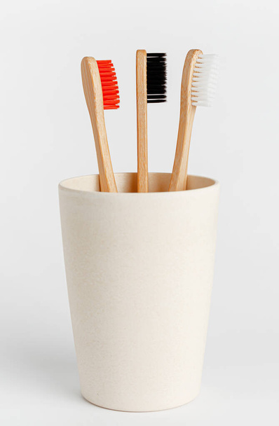Red, white and black bamboo toothbrushes in eco cup on white background. - Photo, image