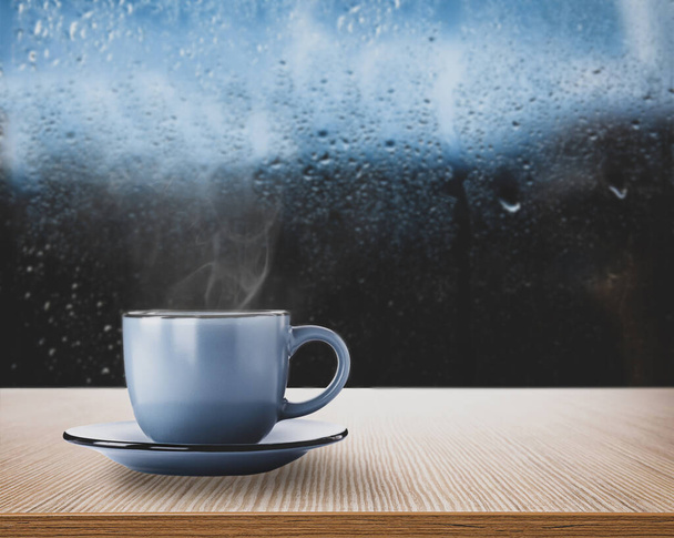 Blue cup with hot beverage near window on rainy day, space for text  - Foto, Imagen