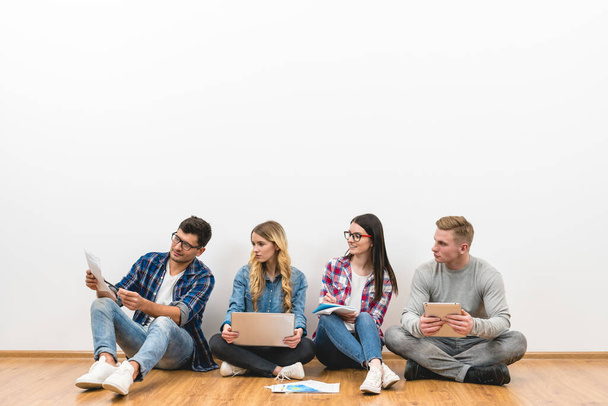 The four young people sit on the floor on the white wall background - Photo, Image