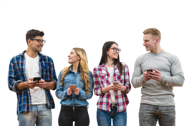 De vier gelukkige mensen met telefoons staan op de witte muur achtergrond - Foto, afbeelding