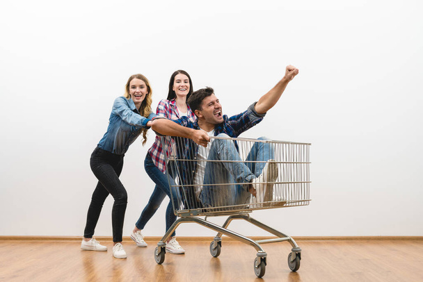 The three people fun with a shopping cart on a white wall background - Foto, Imagen