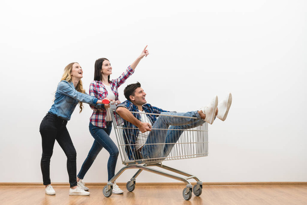 The three happy people with a shopping cart gesture on a white wall background - 写真・画像
