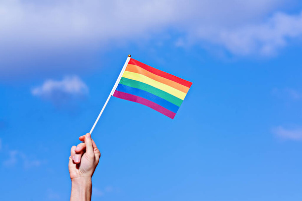 Mavi gökyüzüne LGBTQ gökkuşağı bayrağı sallayarak el kaldırdı. Geleneksel LGBT Onur Kutlaması - Fotoğraf, Görsel
