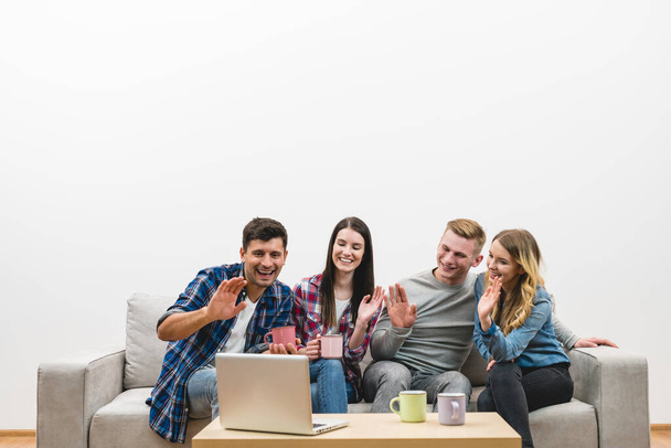 Die vier glücklichen Freunde gestikulieren neben Laptop auf weißem Wandhintergrund - Foto, Bild