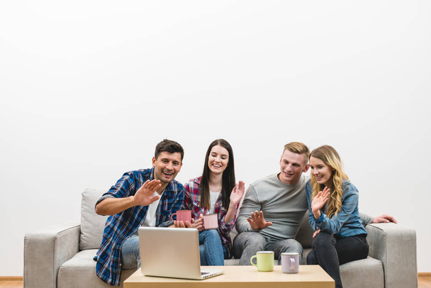 Die vier glücklichen Menschen gestikulieren neben dem Laptop auf dem weißen Wandhintergrund - Foto, Bild