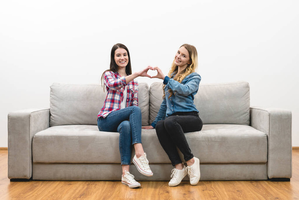 Οι δύο ευτυχισμένες γυναίκες δείχνουν το σύμβολο της καρδιάς στο φόντο του λευκού τοίχου - Φωτογραφία, εικόνα