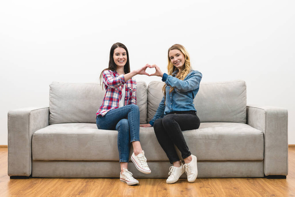 Τα δύο ευτυχισμένα κορίτσια δείχνουν το σύμβολο της καρδιάς στο φόντο του λευκού τοίχου - Φωτογραφία, εικόνα