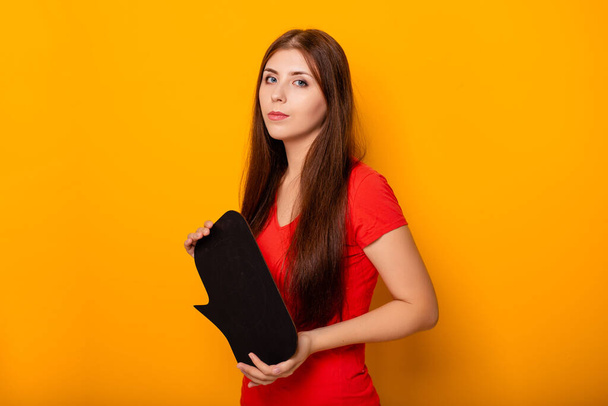 Attractive woman in a red T-shirt is holding a blank board in her hands with space for inscription while standing on a yellow background. - Photo, Image