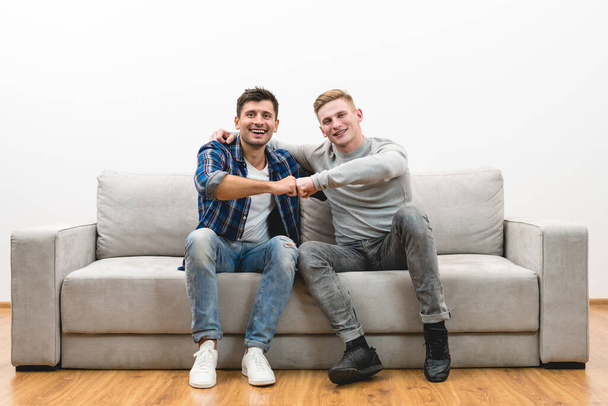 Die beiden glücklichen Männer auf dem Sofa gestikulieren auf dem weißen Wandhintergrund - Foto, Bild